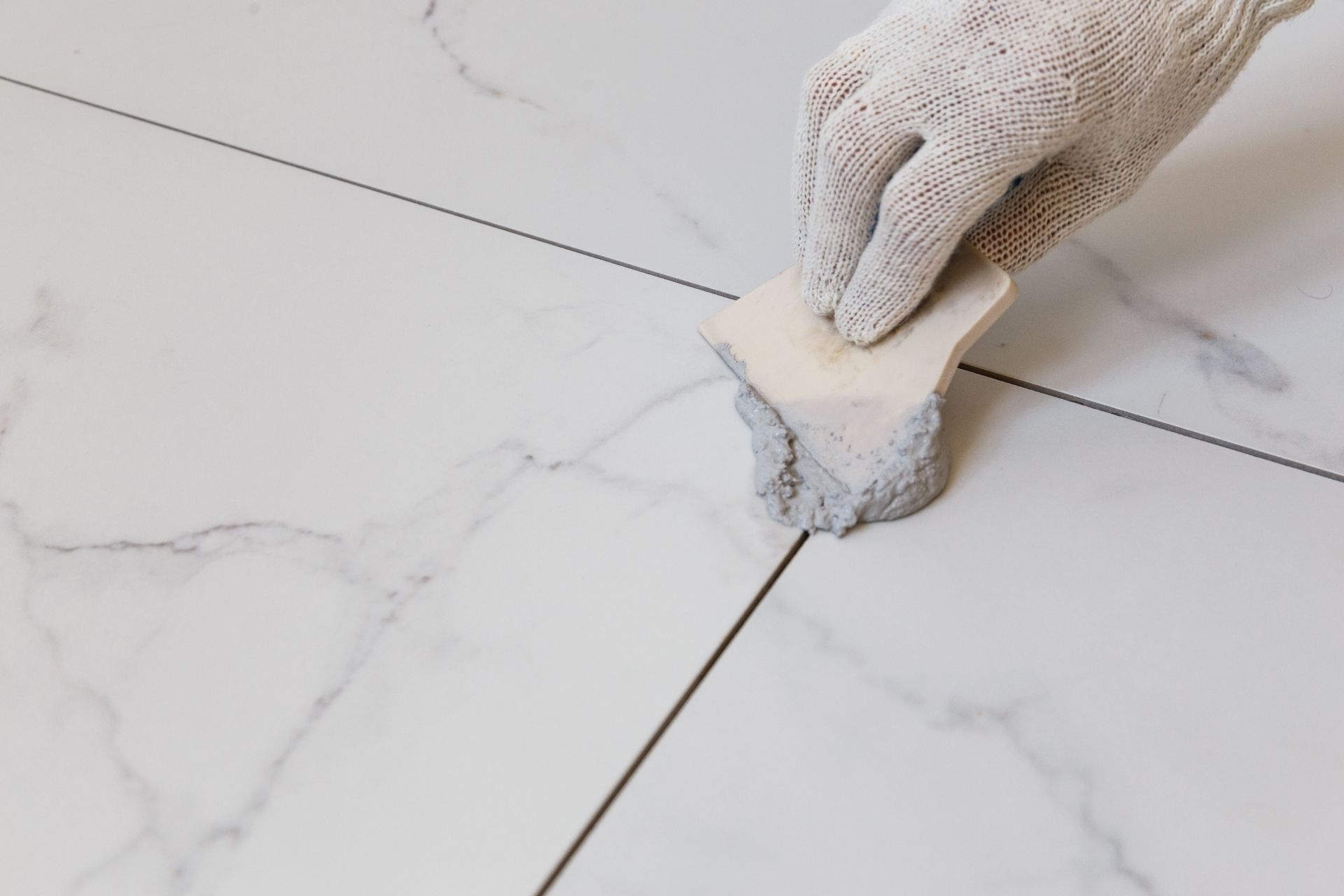 Gloved hand putting grout on white marble floor