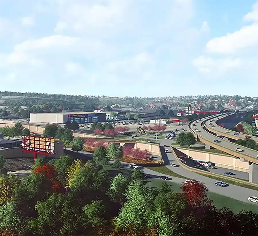 Aerial view of a suburban shopping area with roads, buildings, and green trees under a partly cloudy sky