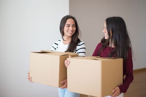 Two women holding cardboard boxes and smiling in a bright indoor room