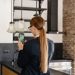 Person using a smartphone in a modern kitchen while facing the counter and hanging lights
