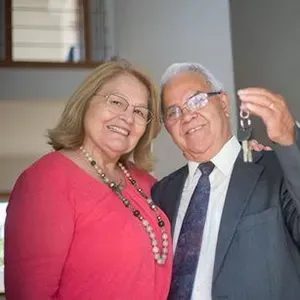 Two smiling adults in formal attire, posing indoors; one holds up a set of keys.