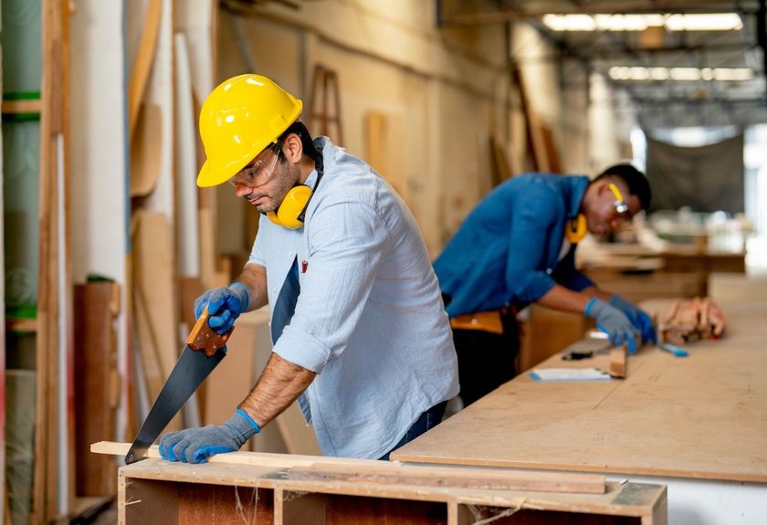 Workers in hard hats sanding a large wooden surface in an industrial workshop