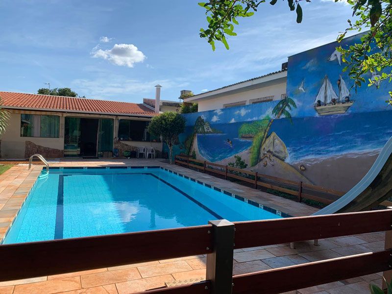 Uma piscina retangular com água azul brilhante fica em um pátio ao lado de uma parede pintada com um mural costeiro.
