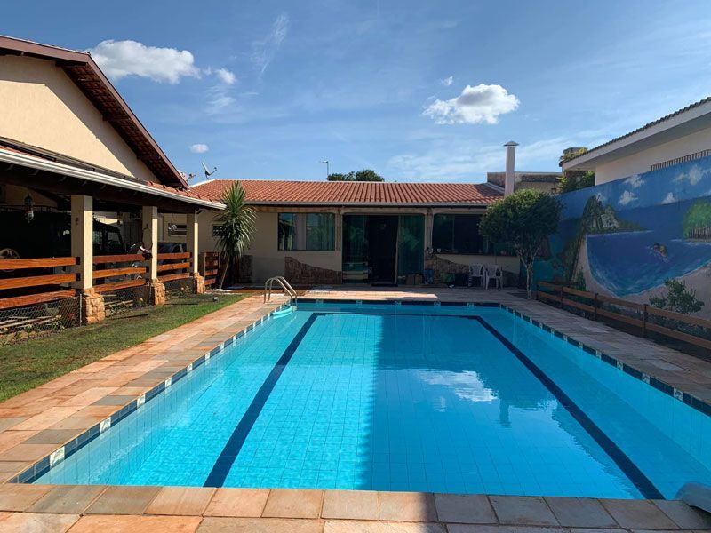 Uma piscina retangular com água azul está localizada em um pátio entre uma casa e uma parede pintada com um mural de temática litorânea.