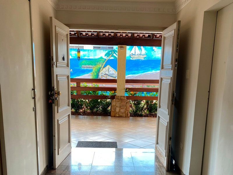 Uma porta dupla aberta revela um pátio revestido com azulejos, apresentando um vibrante mural com tema de praia e uma cerca de madeira.