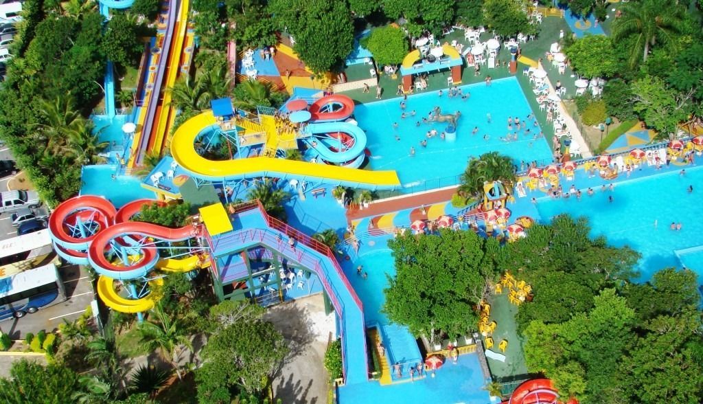 Vista aérea de um parque aquático colorido com várias piscinas, toboáguas vibrantes e uma exuberante vegetação ao redor.