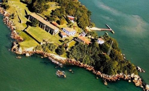 Vista aérea da Ilha Goat em Newport, Rhode Island, com seus edifícios históricos de pedra, gramados verdes e um cais de madeira.