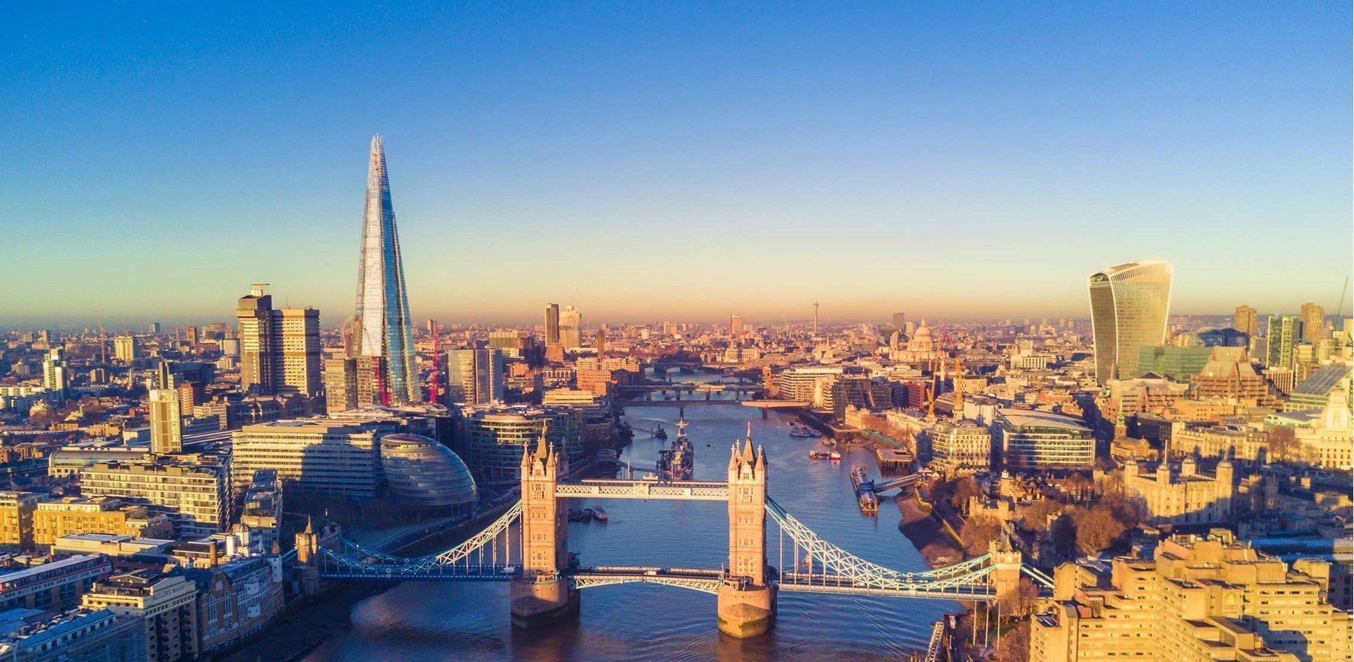 Vista aérea de Londres ao pôr do sol, com a Tower Bridge sobre o rio Tâmisa e o arranha-céu The Shard.