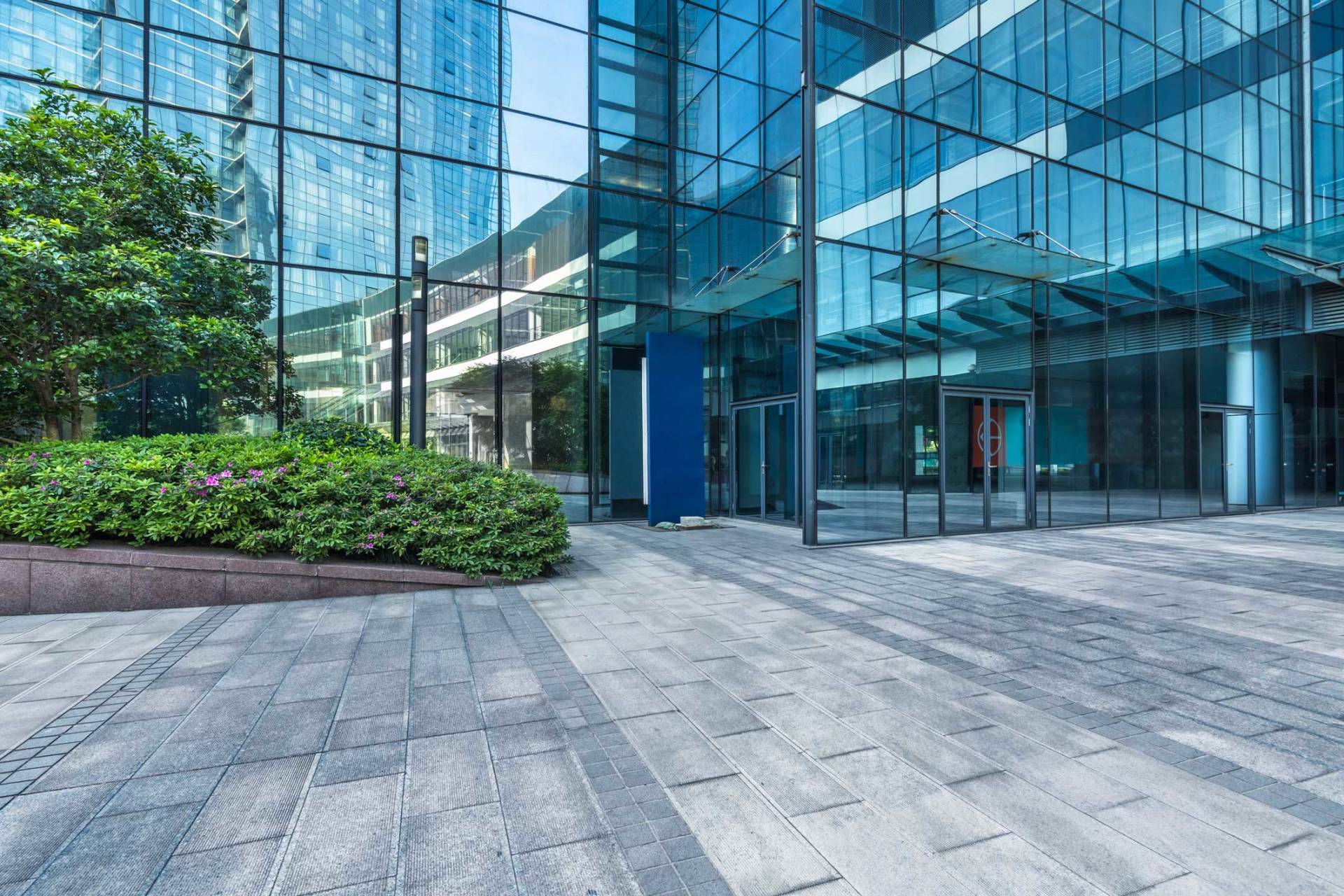 A large glass building with a brick walkway in front of it.