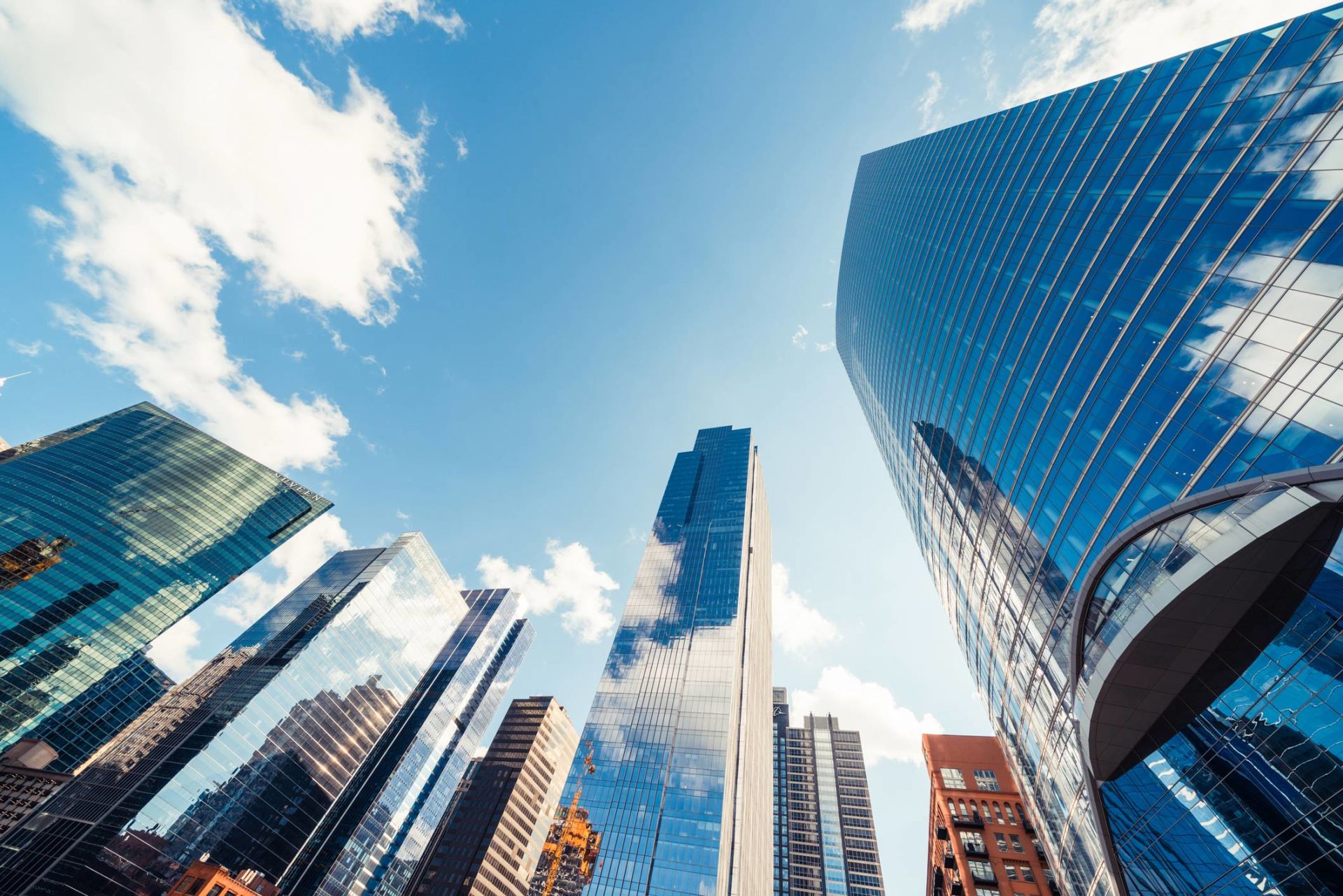 Looking up at a city skyline with a blue sky and clouds in the background.