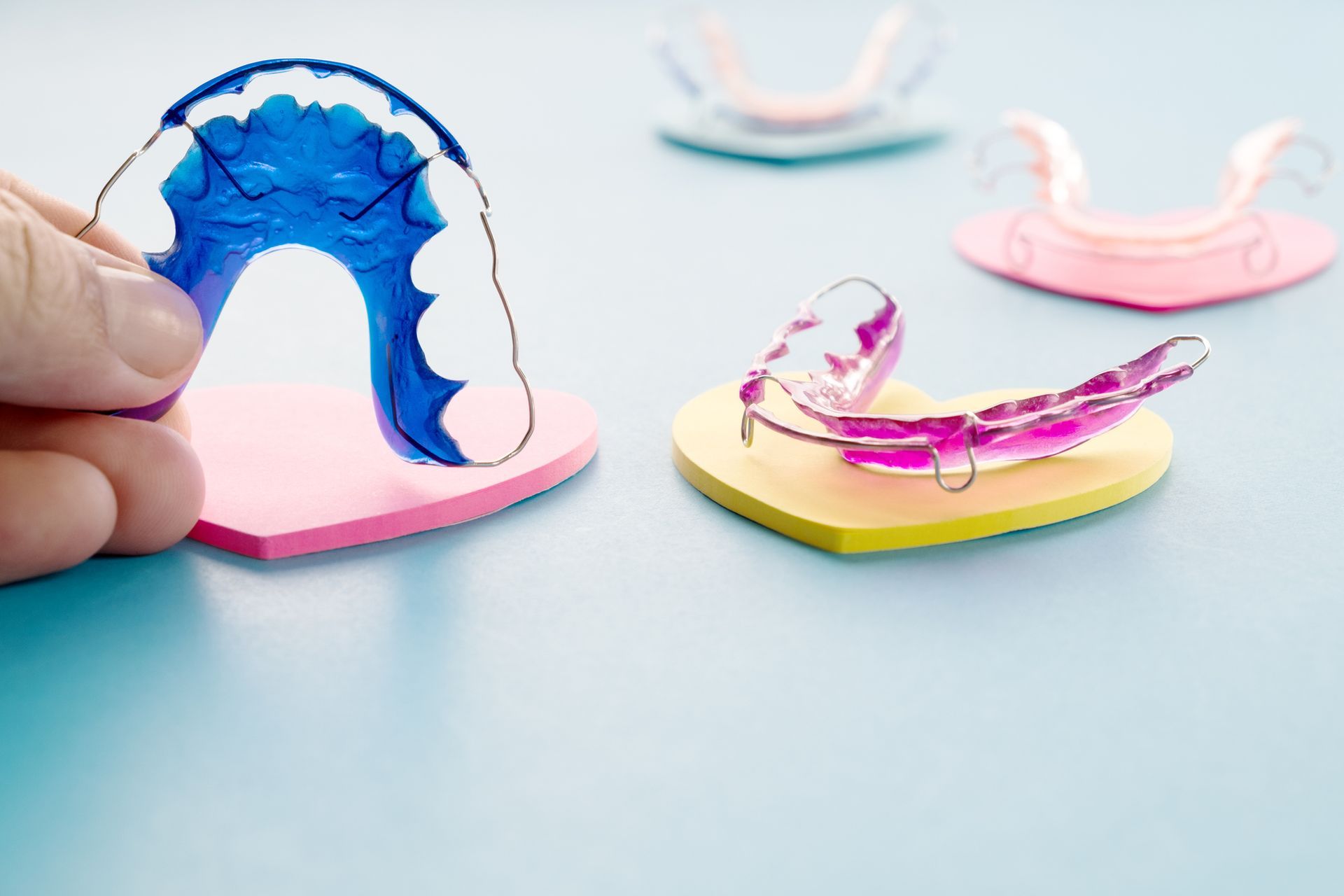 Hand holding blue retainer over pink heart, with other retainers on colored hearts.