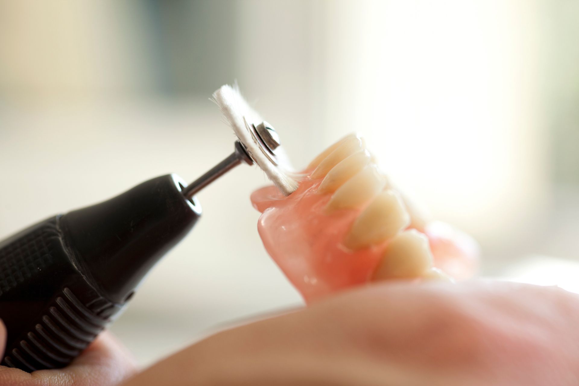 A dentist using a rotary tool to adjust a pink-based denture with artificial teeth.