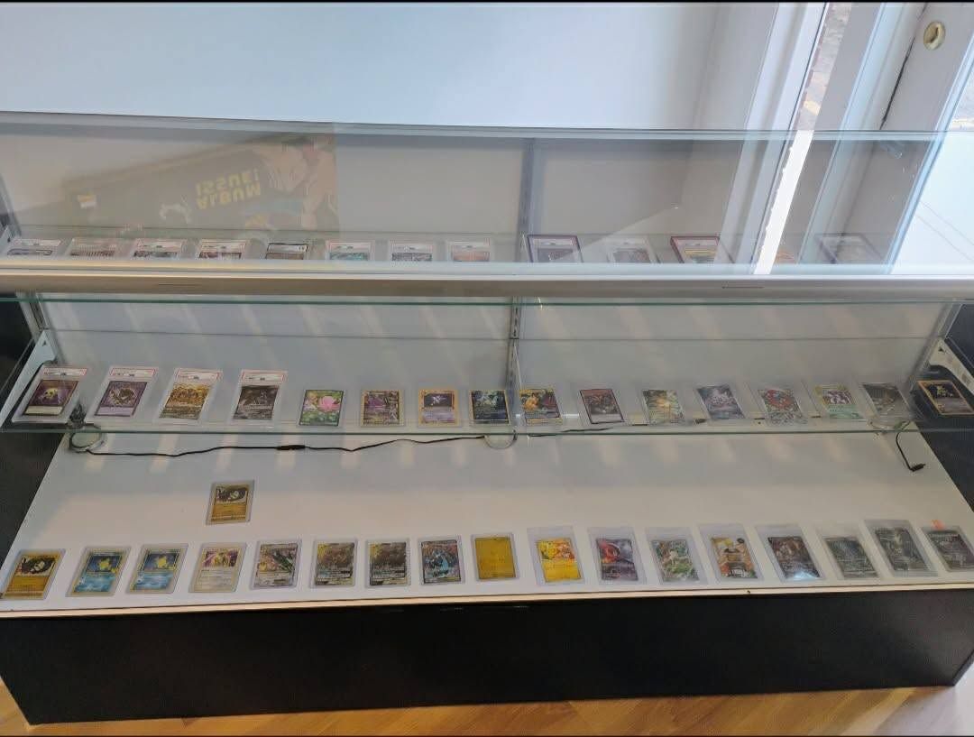 Glass display case with rows of small trading cards arranged on shelves in a bright room