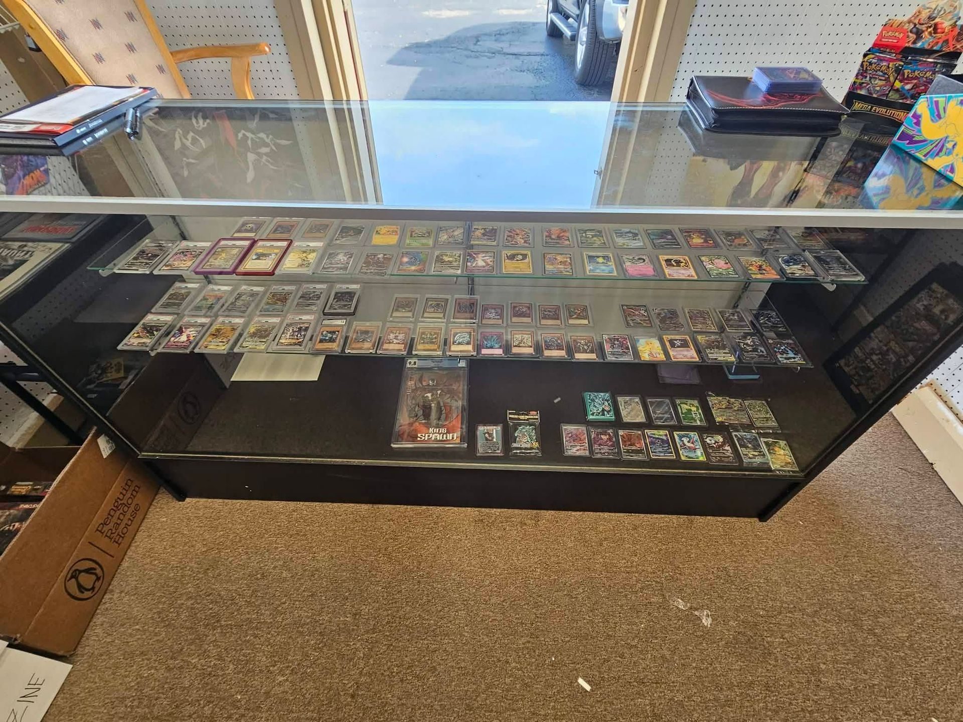 Glass display case filled with trading cards in a shop, with boxes and shelves around it