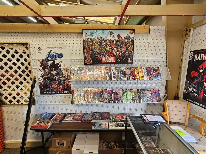 Comic book display on shelves and tables in a pegboard-walled booth with posters and colorful merchandise.
