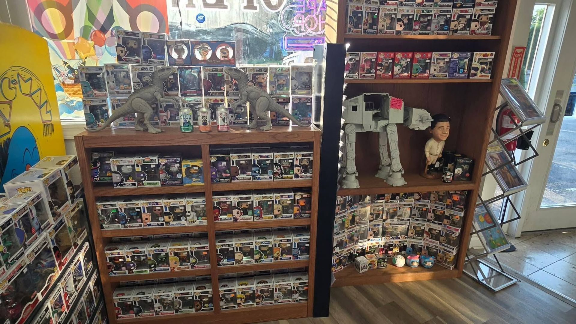 Toy store shelves filled with colorful collectible figures and boxed items, with a display cabinet on the right.
