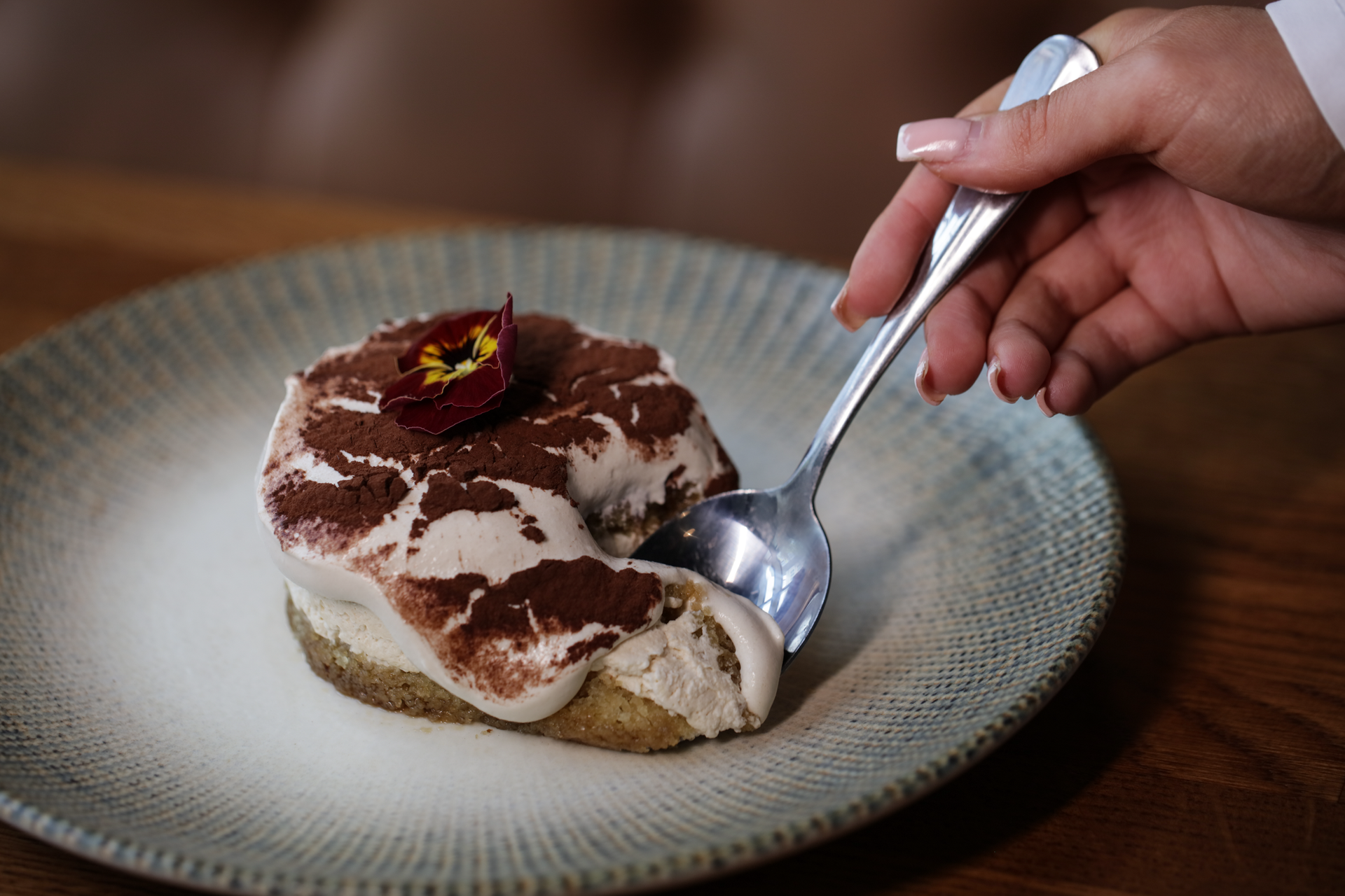 Hand holding a spoon over a slice of chocolate dessert on a plate