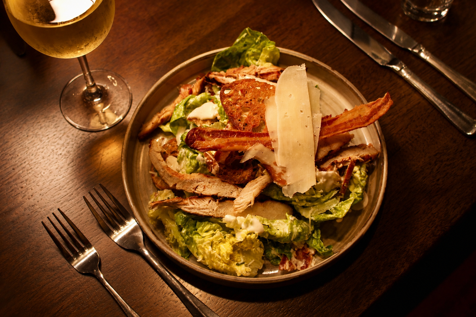 Salad bowl with grilled chicken and cheese on a wooden table beside a glass of wine