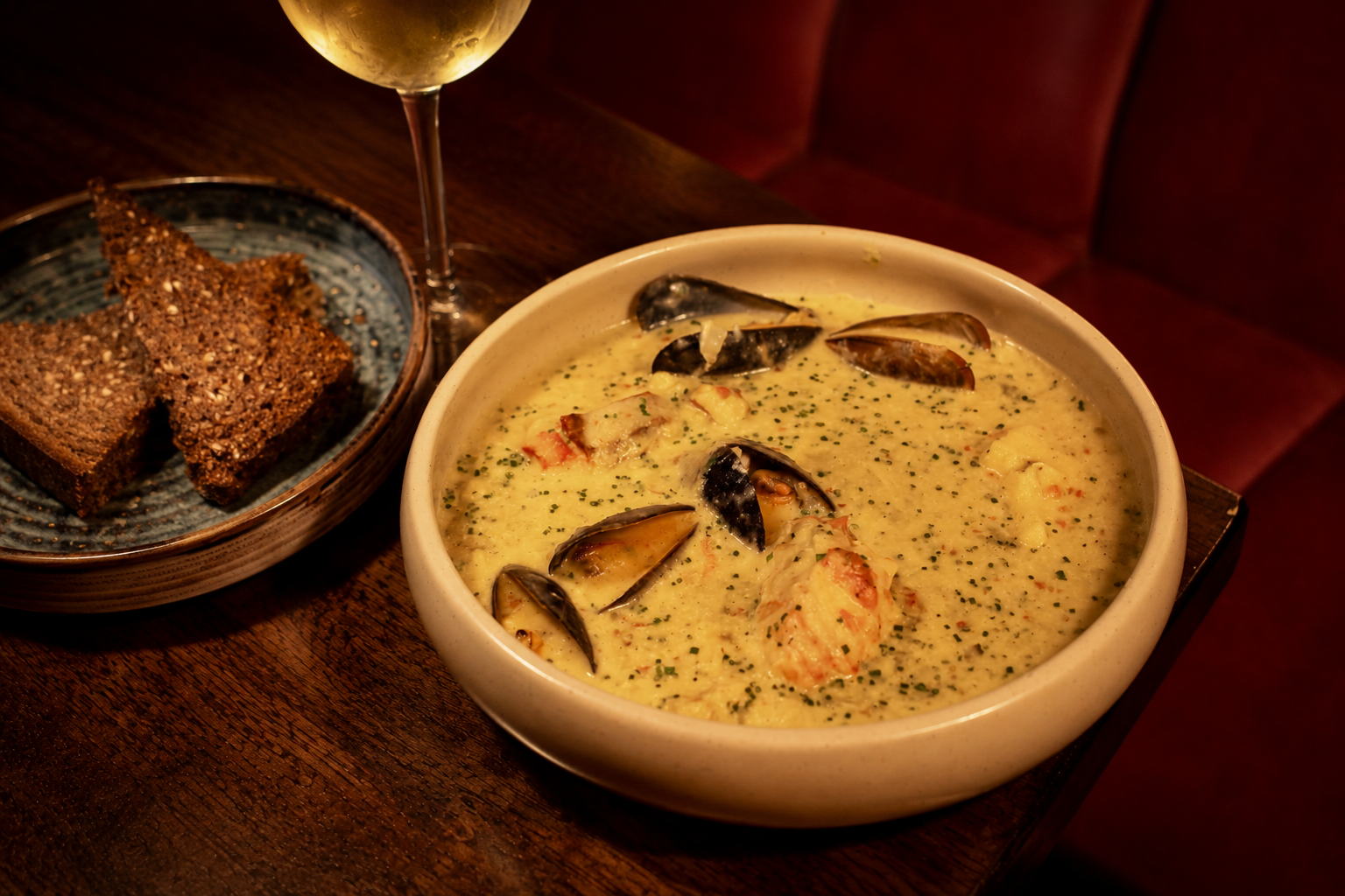 Creamy chowder in a white bowl beside toasted bread on a dark table