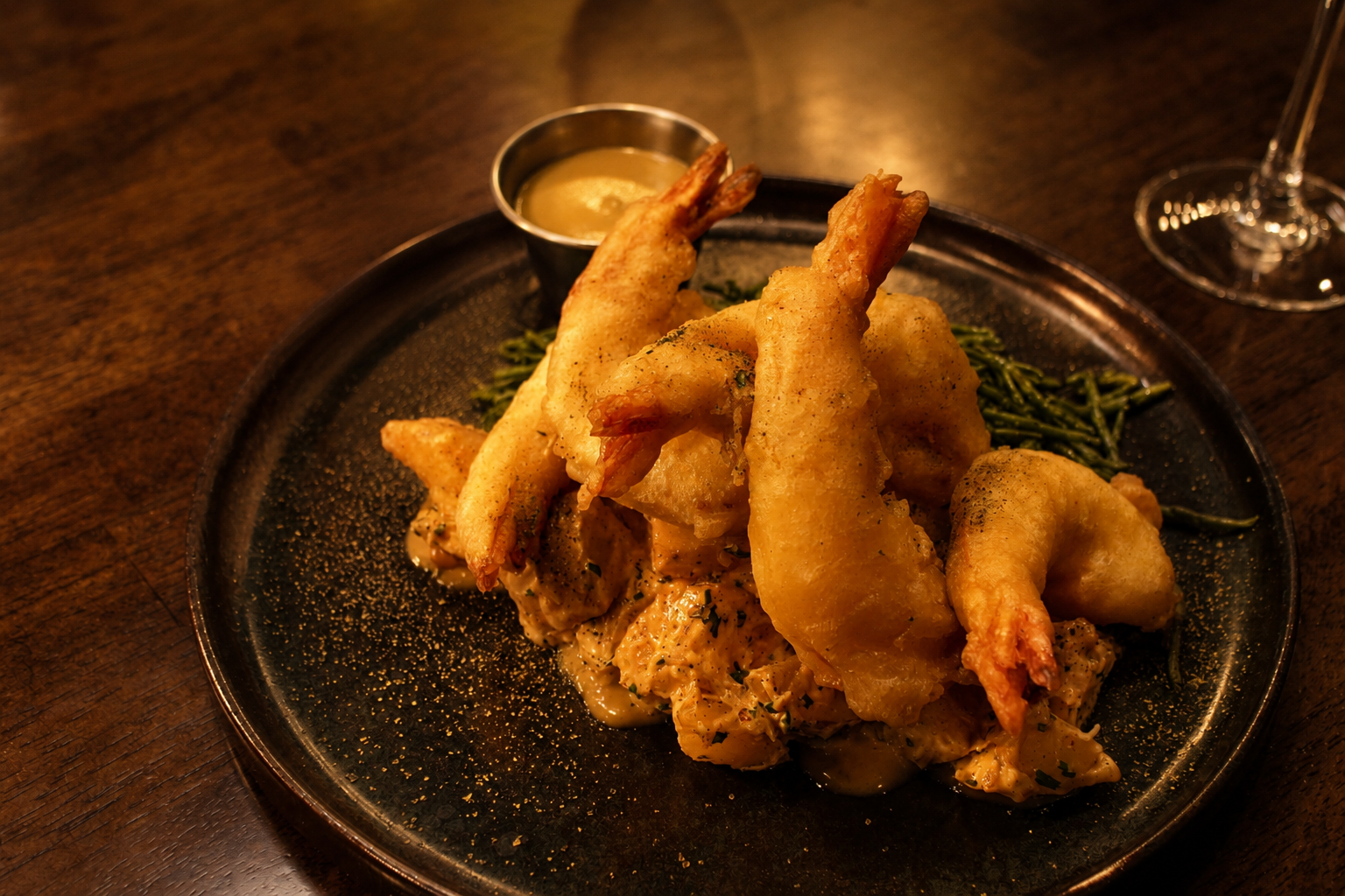 Plate of fried prawnand fries on a dark table with dipping sauce and rosemary garnish
