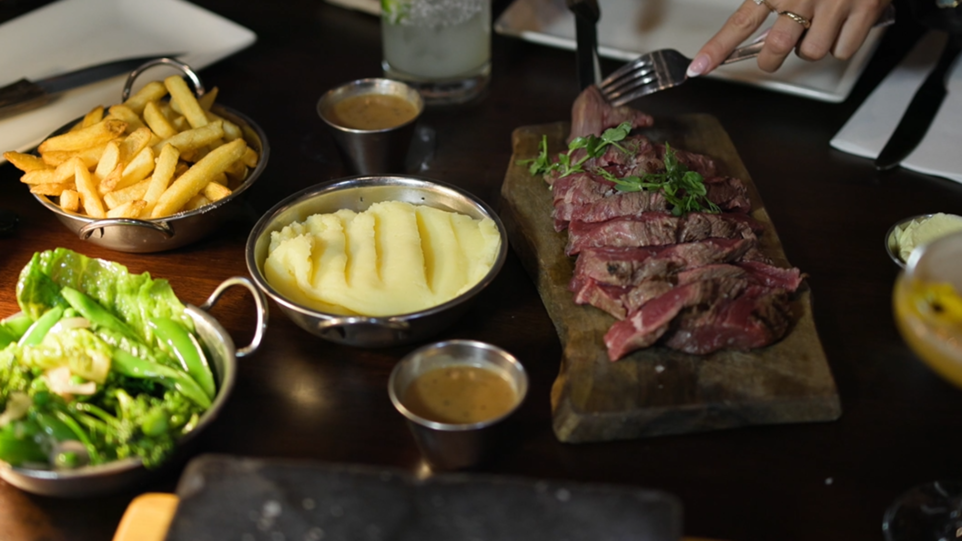 Steak platter with sauces, mashed potatoes, fries, and salad on a restaurant table