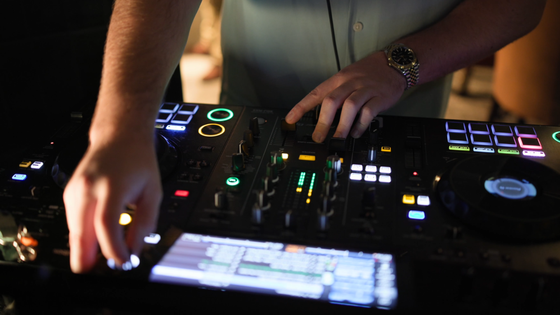 DJ using a mixing console with glowing controls and a laptop in a dimly lit room