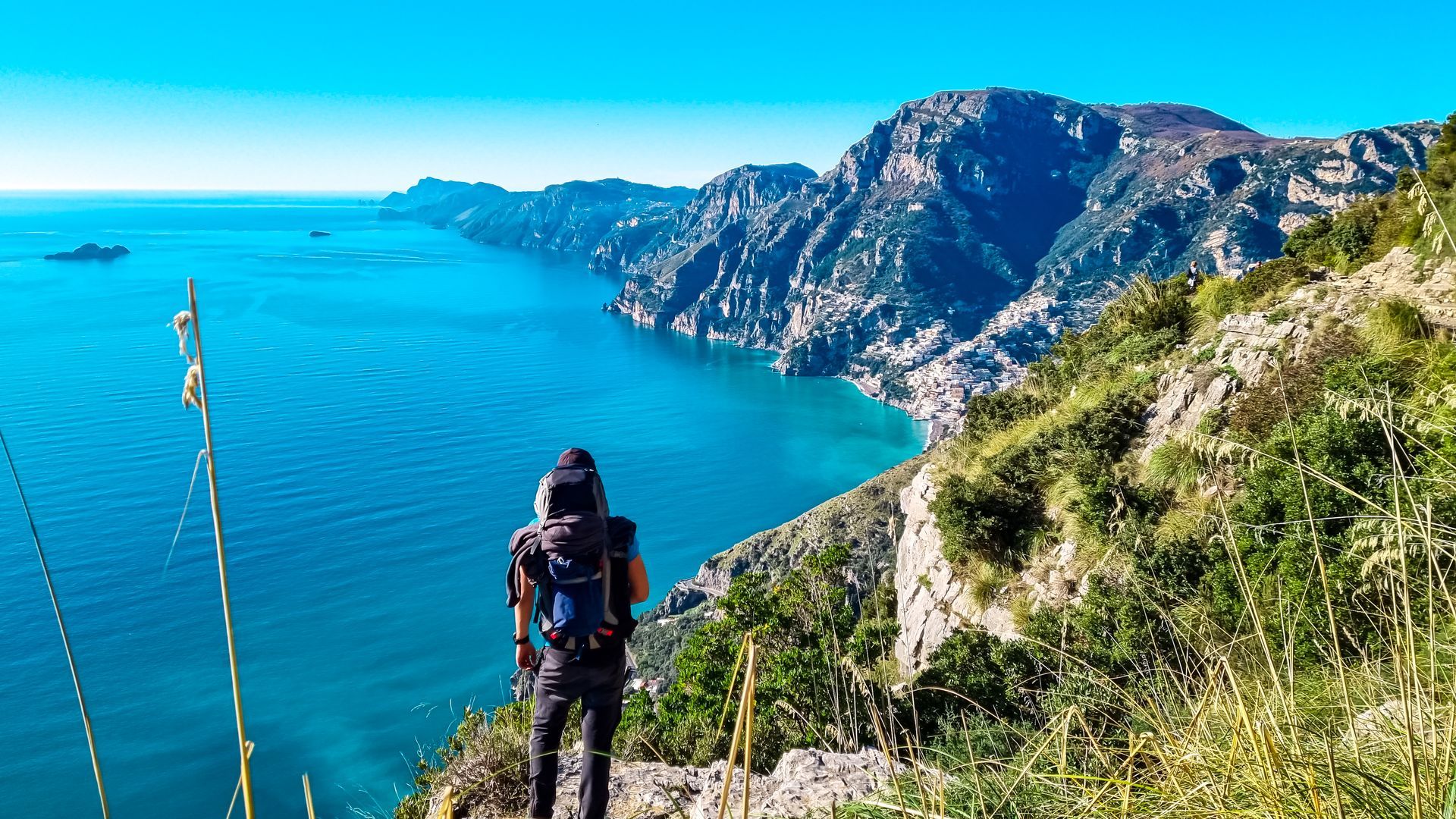 Persona che guarda verso un mare turchese e una costa frastagliata, con un cielo azzurro e limpido sopra.