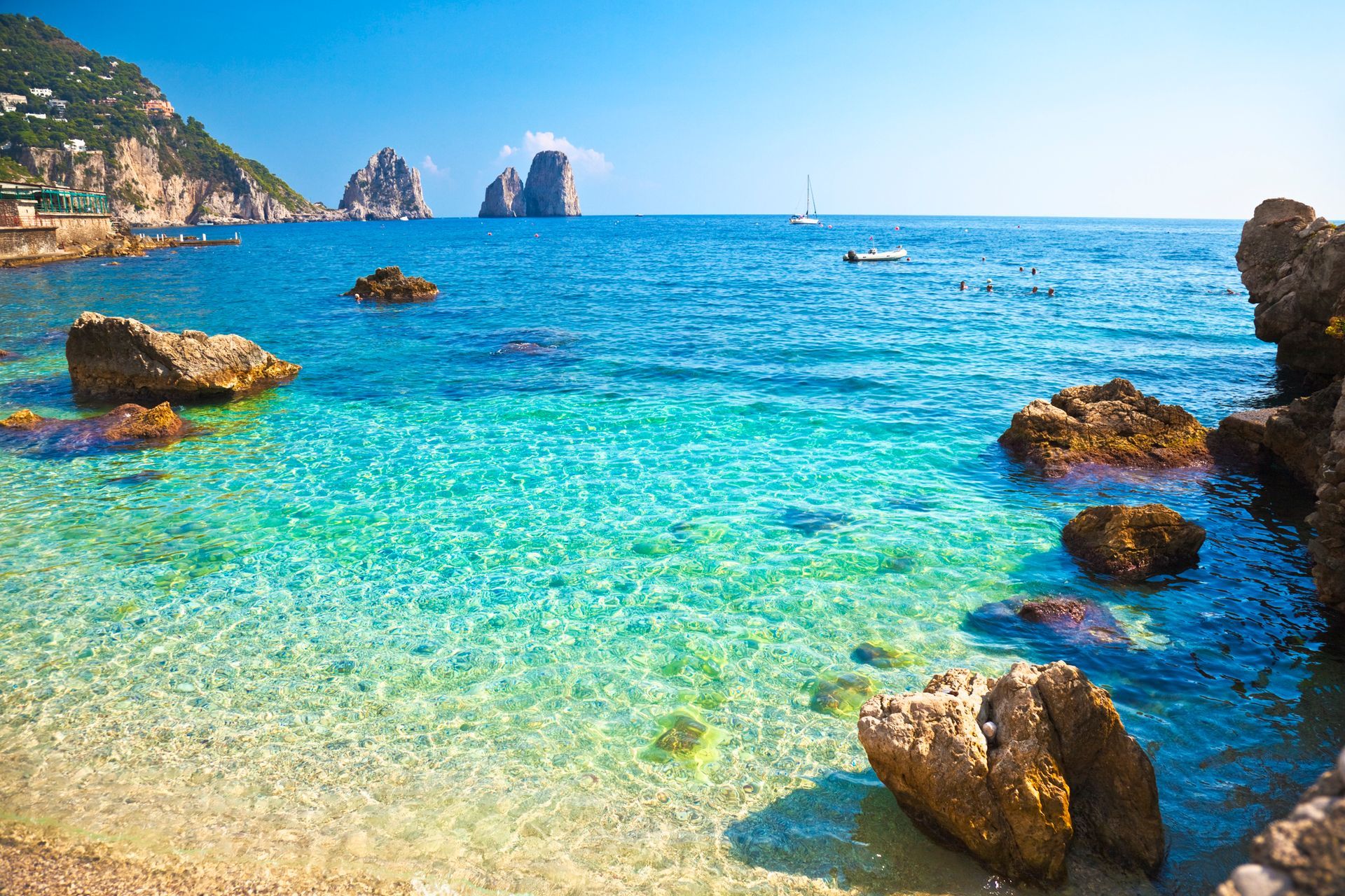 Mare turchese brillante con rocce e un'isola lontana, sotto un cielo azzurro e limpido.