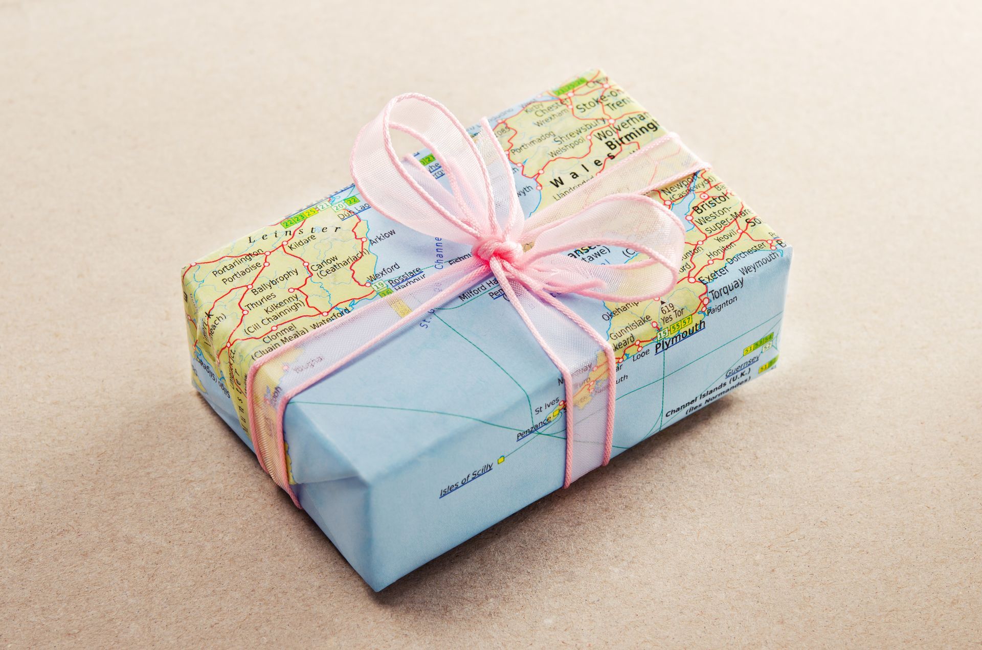 Scatola regalo avvolta in una mappa con un nastro rosa legato intorno, appoggiata su una superficie di colore chiaro.