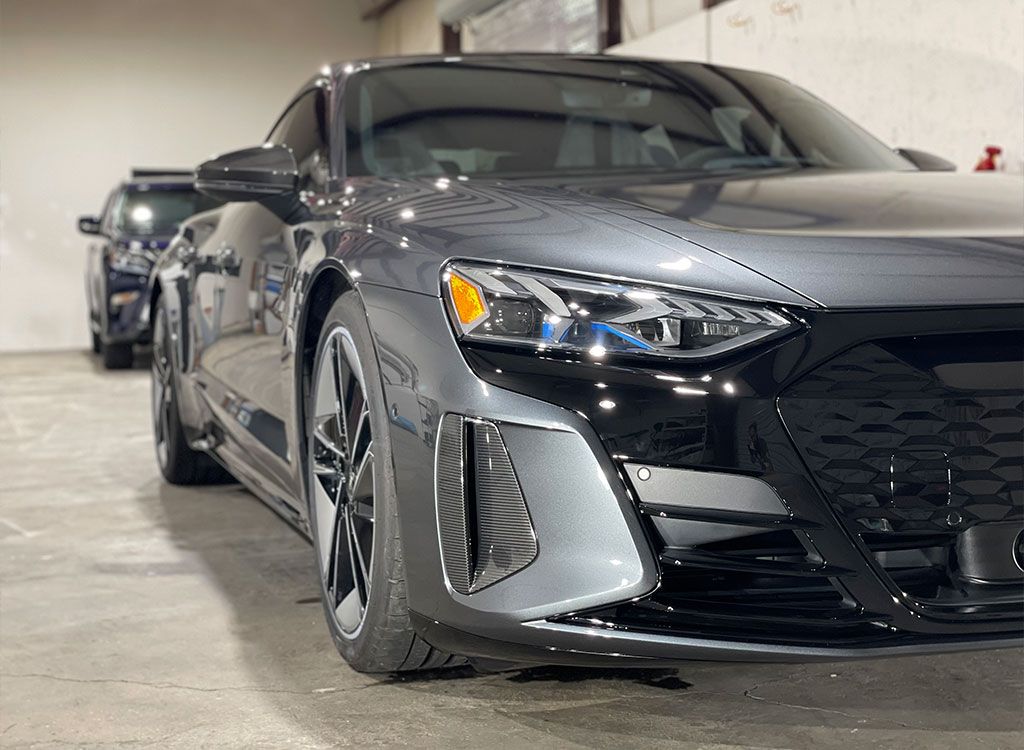 A black car is parked in a garage next to another car.