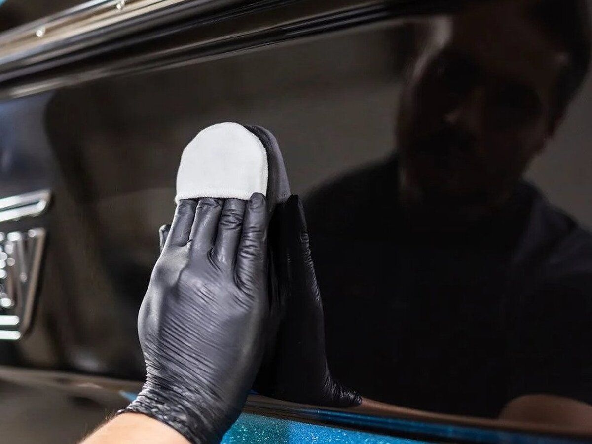A person wearing black gloves is cleaning a car window with a sponge.