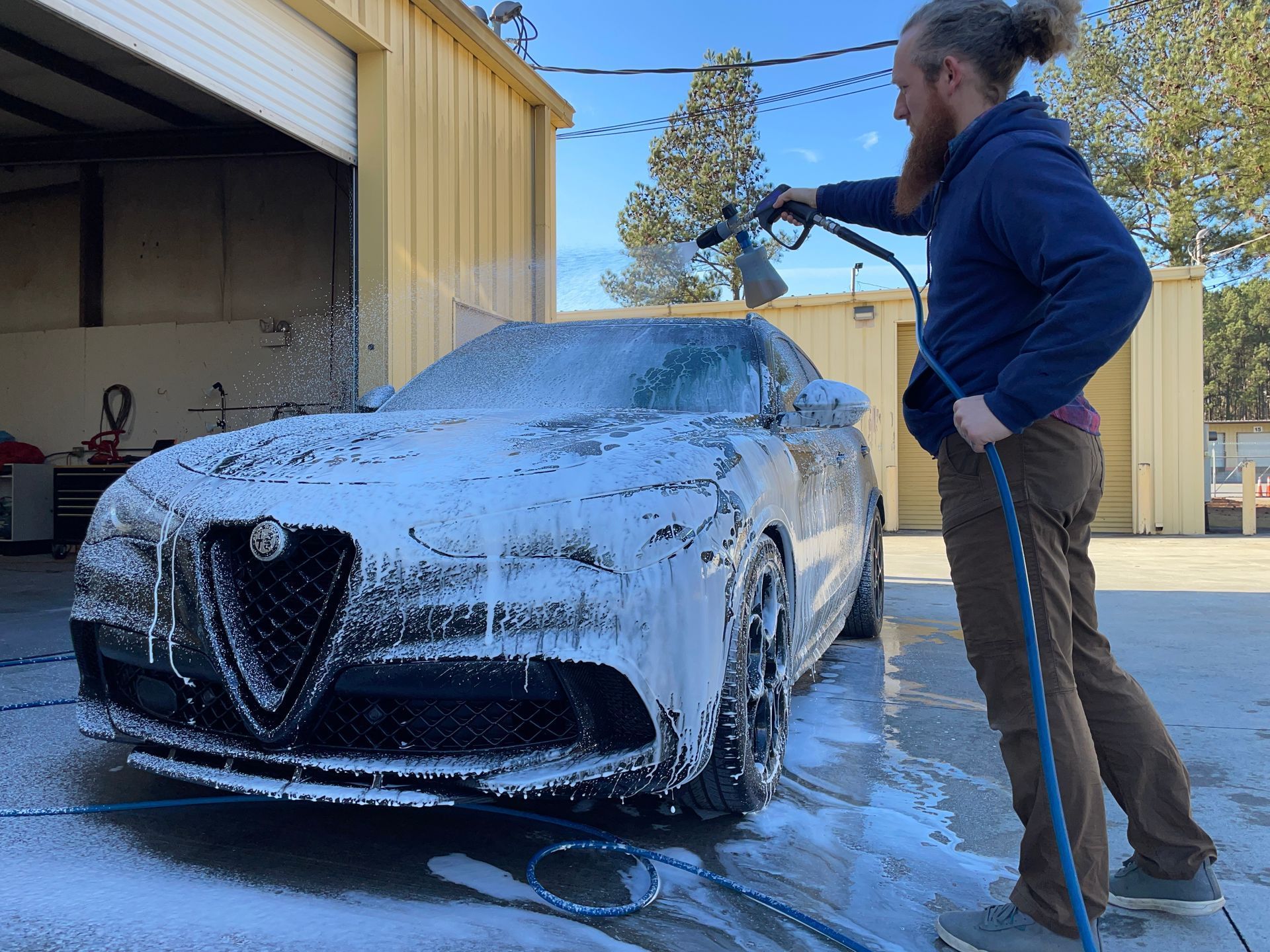 A man is washing a car with a hose and foam