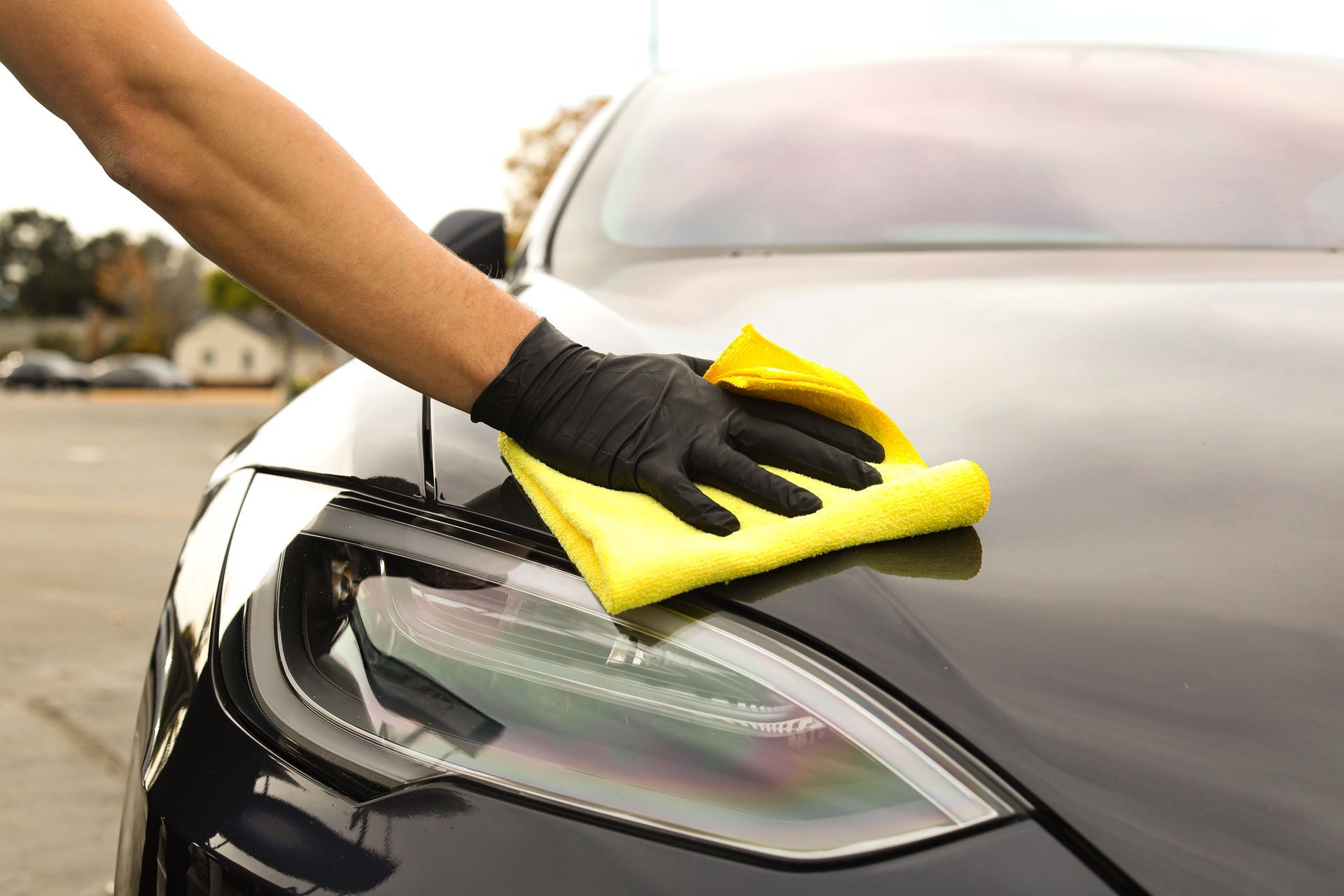 Person in black gloves wiping a black car with a yellow cloth.