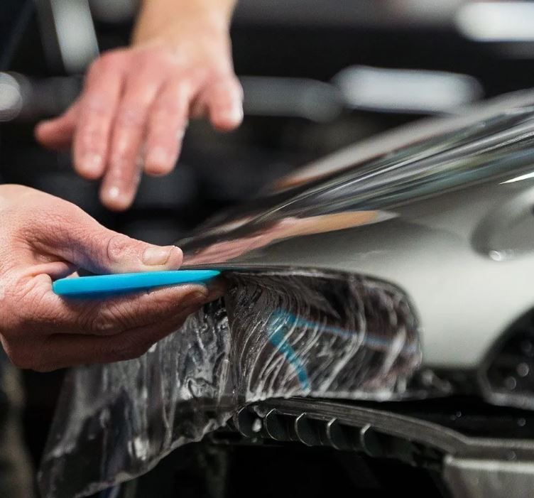 A person is wrapping a car with plastic wrap.