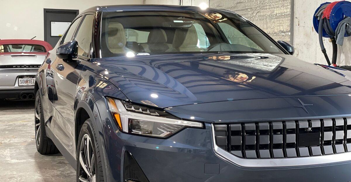A blue car is parked in a garage next to another car.