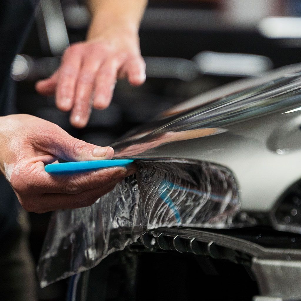 A person is wrapping a car with plastic wrap.