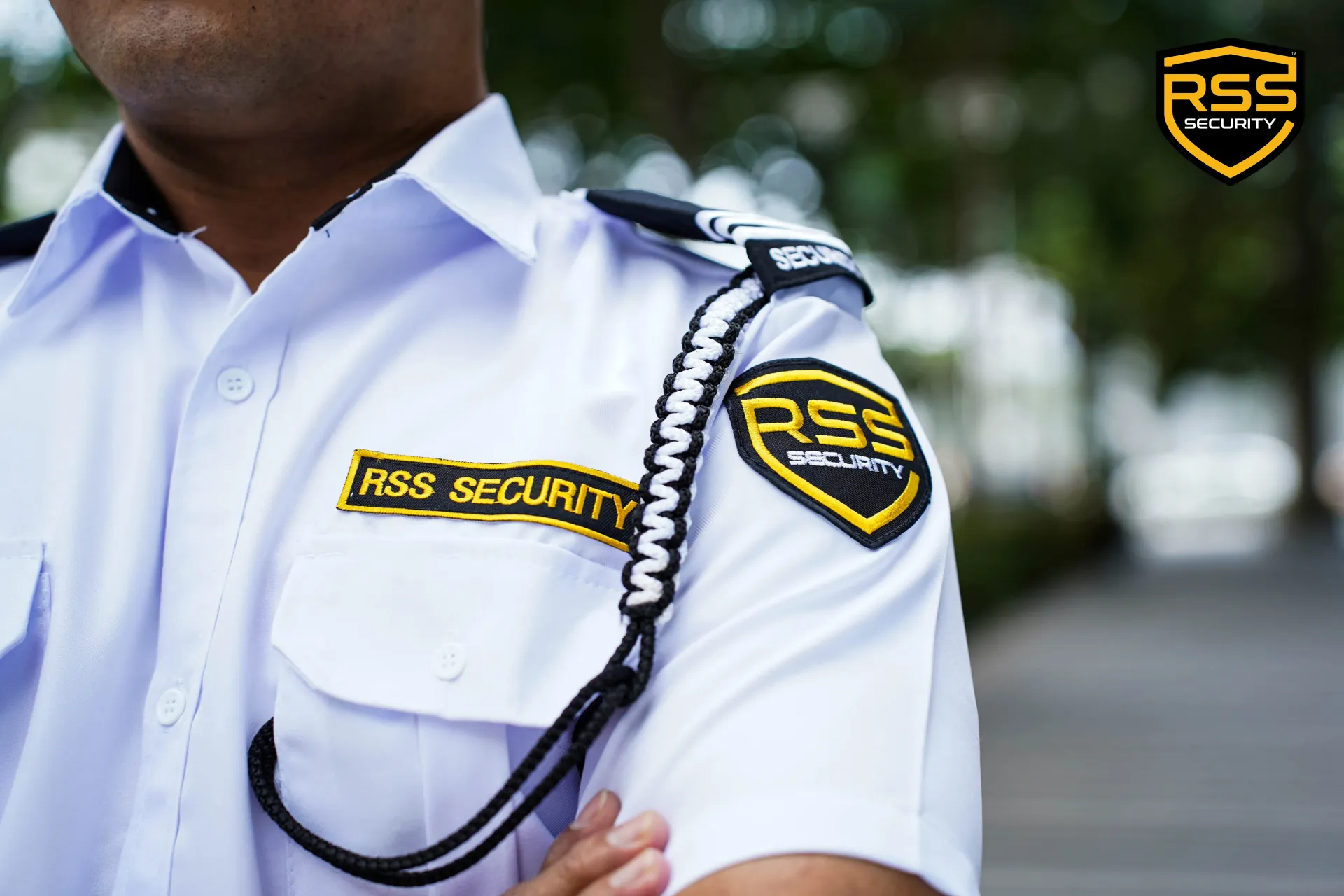 Security guard in white uniform with RSS patches and shoulder cord, standing outdoors.