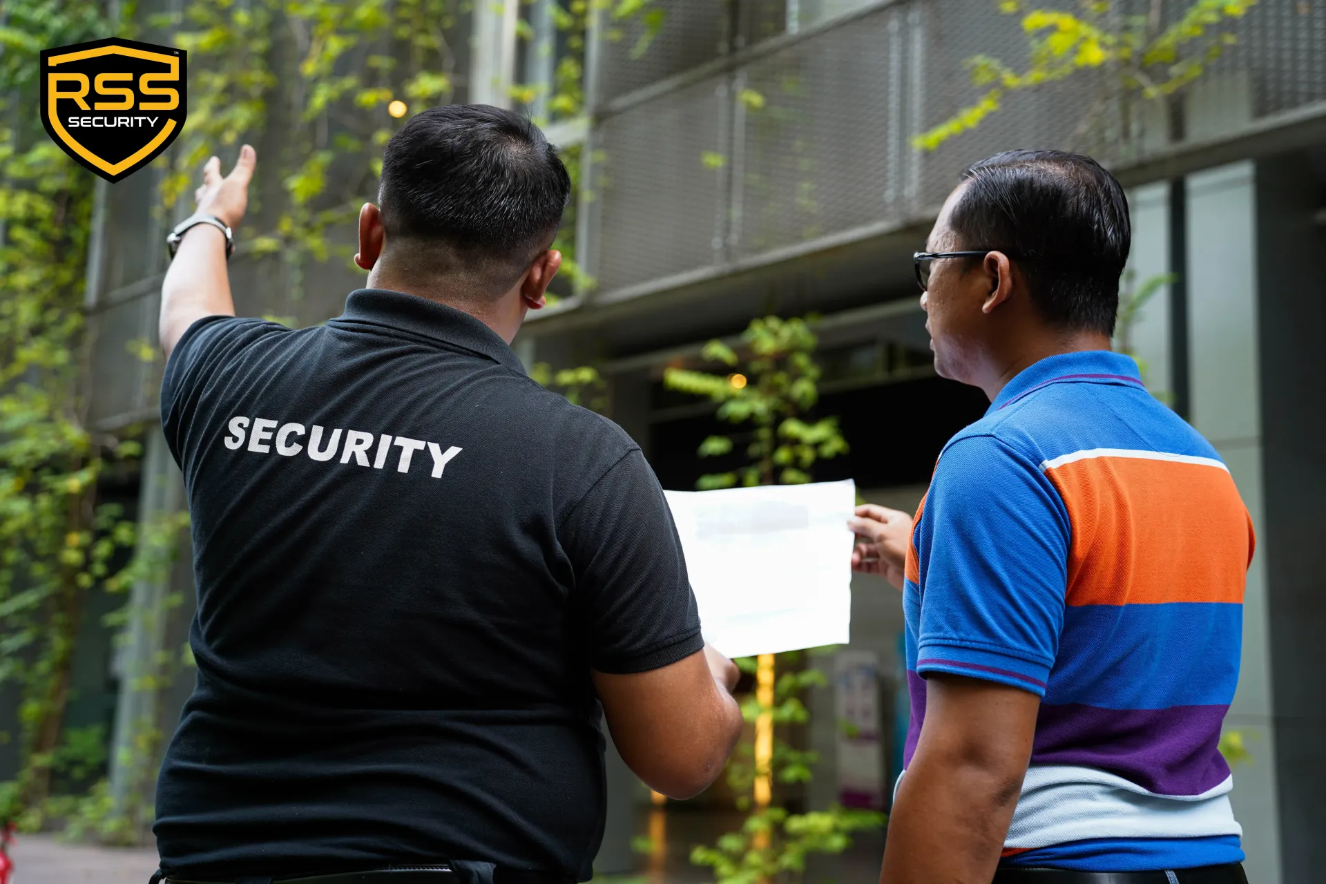 Security guard holding a paper while speaking with a man outside a building