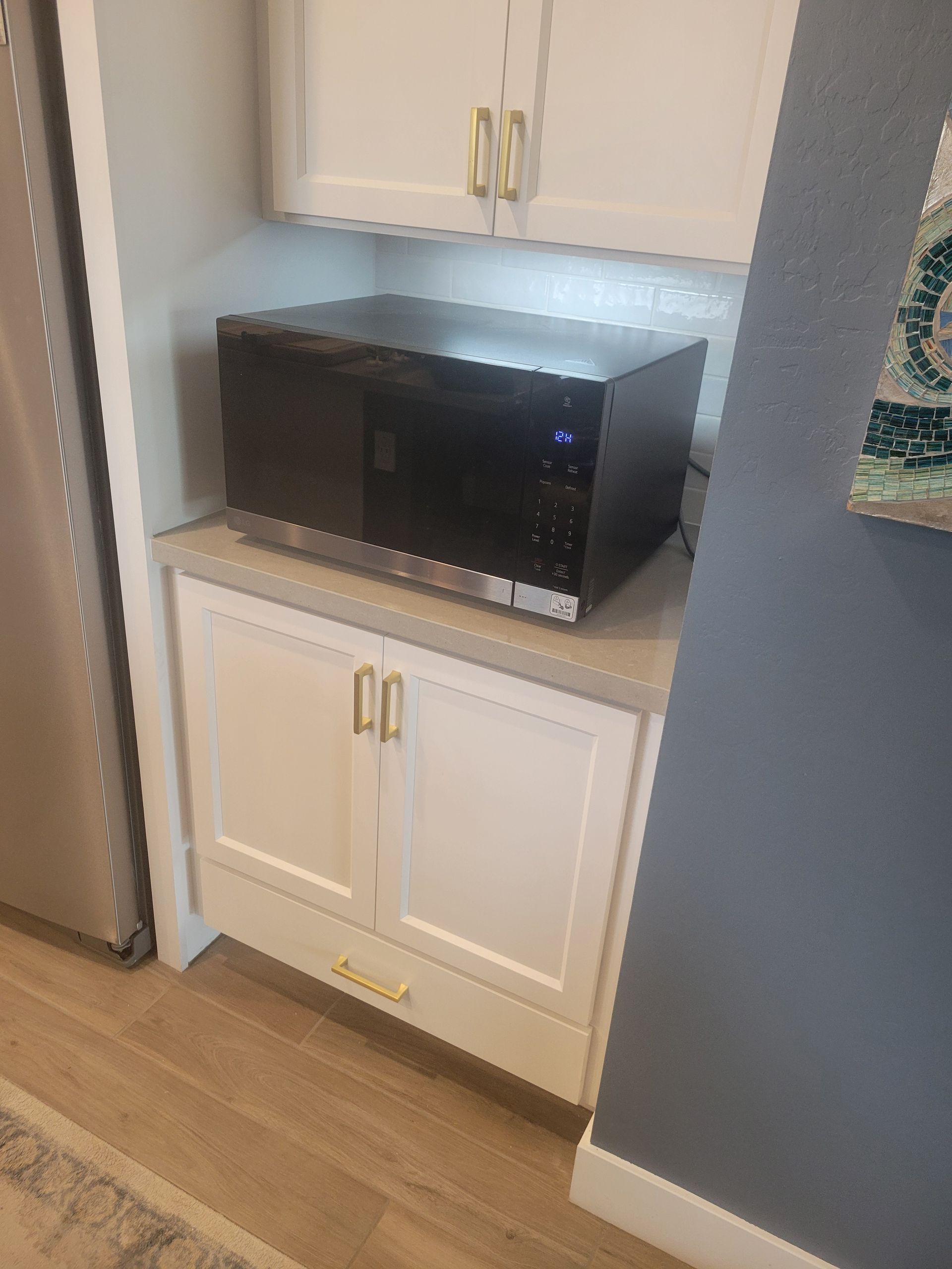 White cabinetry with a microwave built-in, gold hardware, and a countertop.