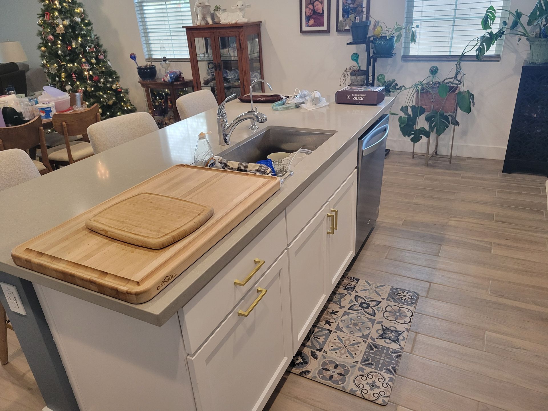 Kitchen island with cutting boards, sink, and dishwasher. White cabinets with gold handles. Tile floor.