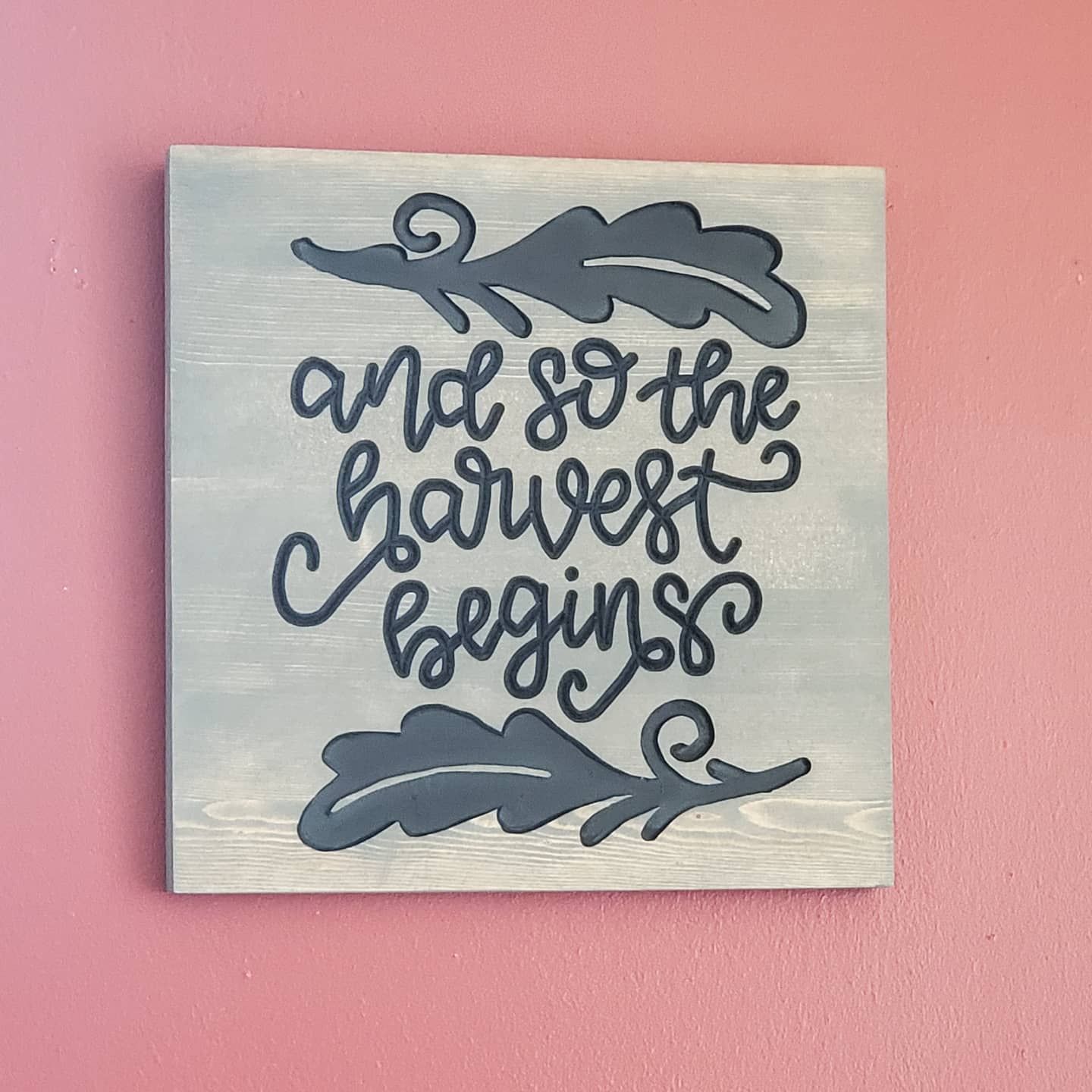 Gray wooden sign with black lettering and leaf accents that reads,