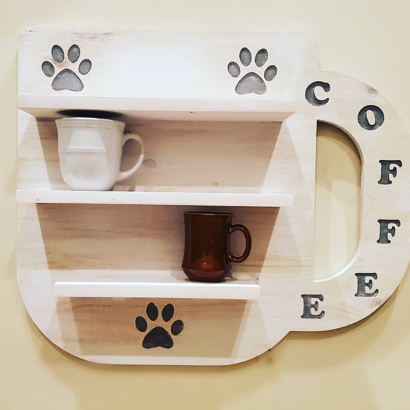 Wooden coffee mug-shaped shelf with paw prints, displaying mugs.