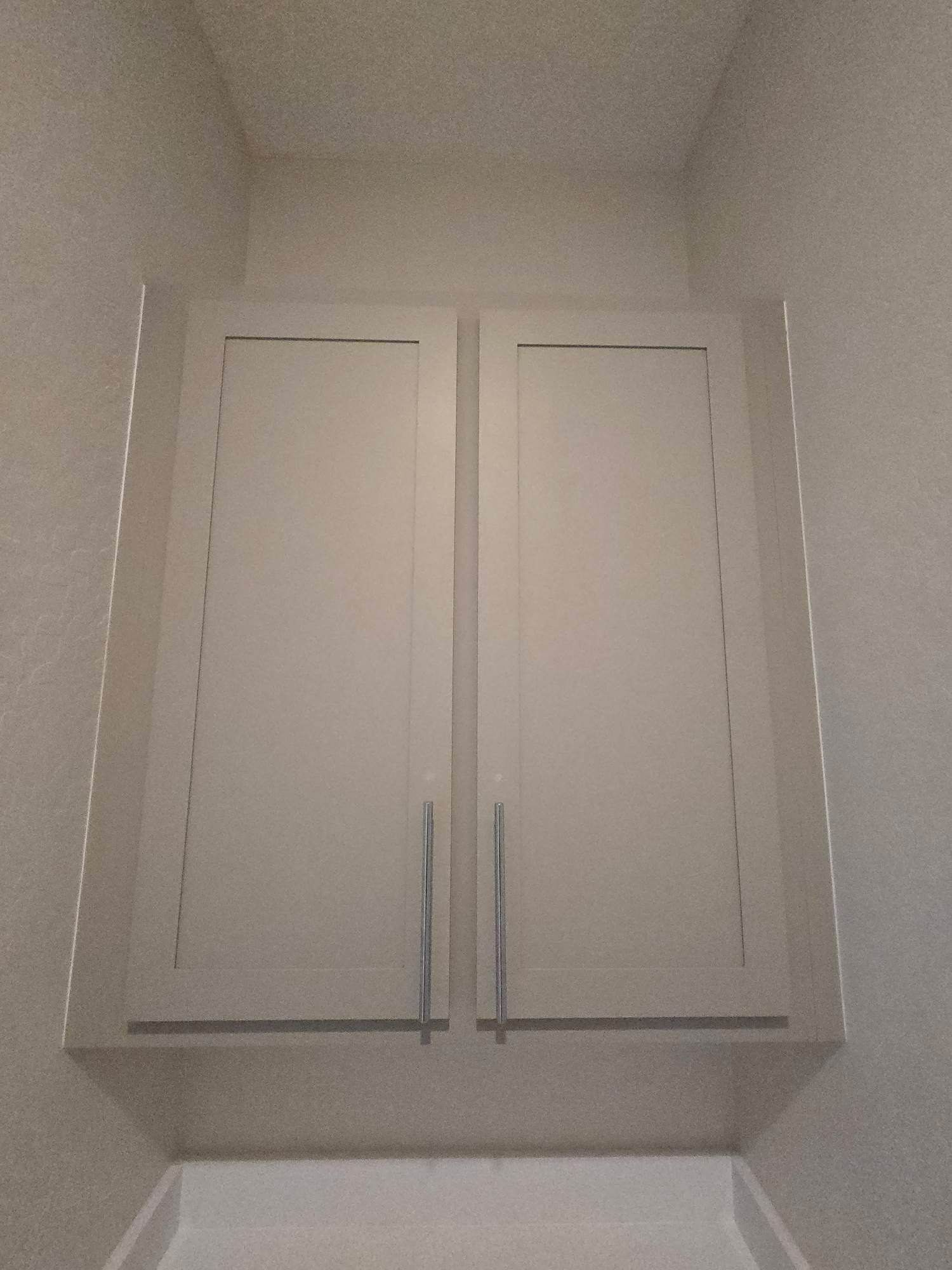 White upper cabinet with two doors and silver handles, mounted above a lower cabinet.