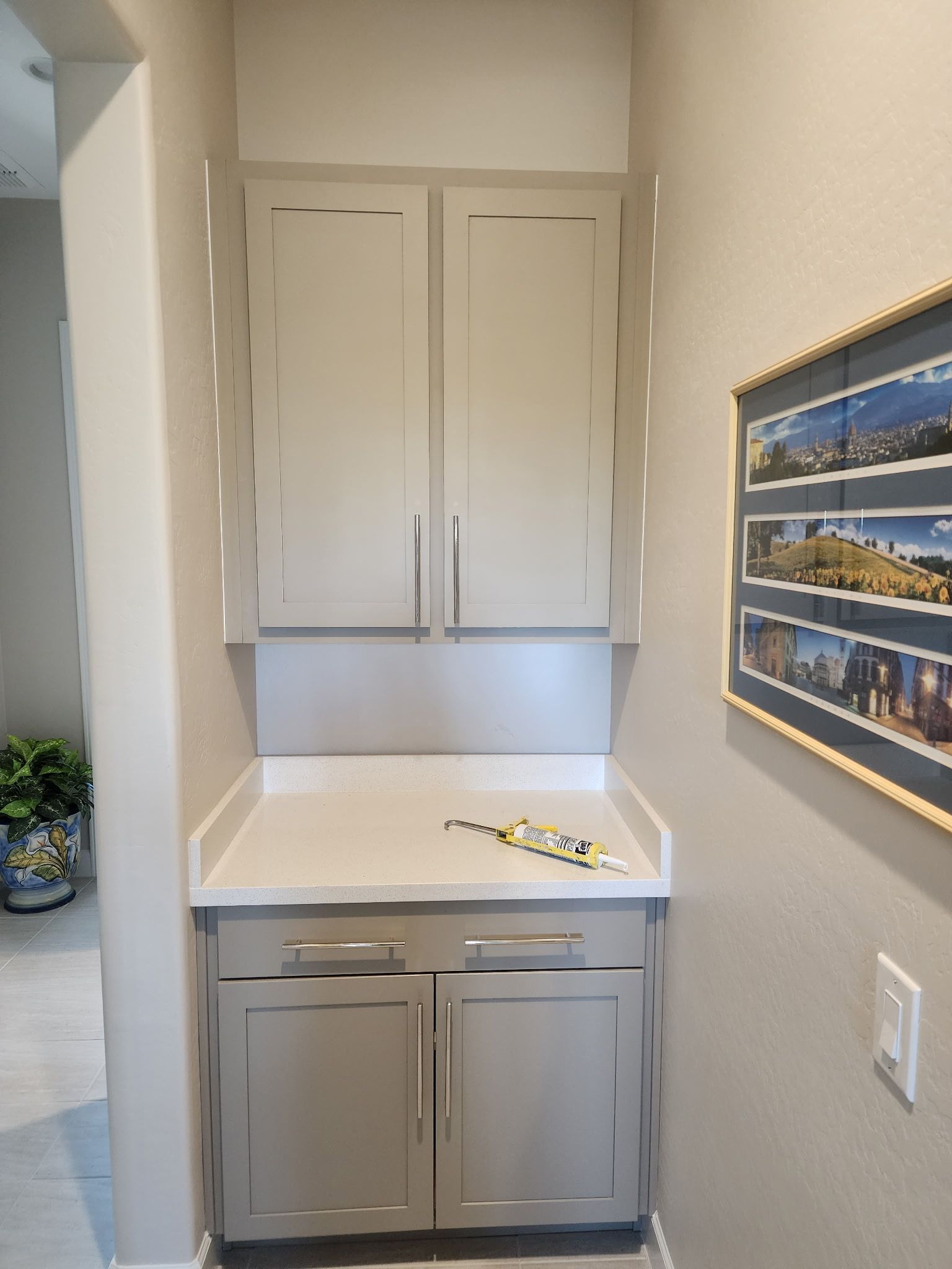 Built-in light gray cabinetry with a countertop, located in a narrow hallway; a framed picture hangs nearby.