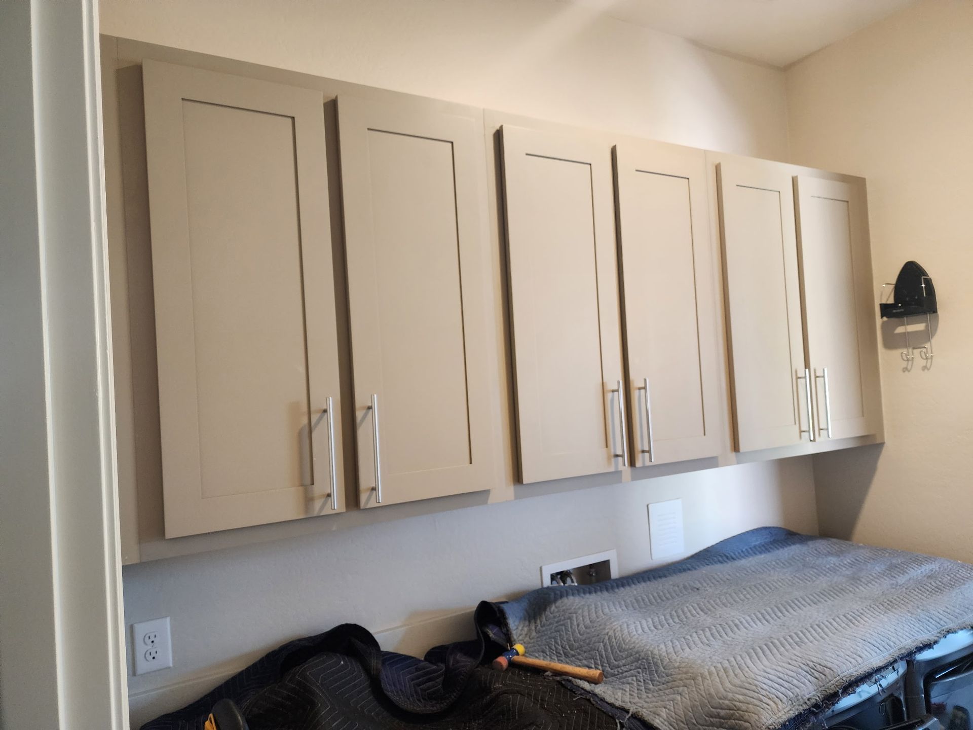 Six tan storage cabinets above a laundry area with a gray blanket on the washer.