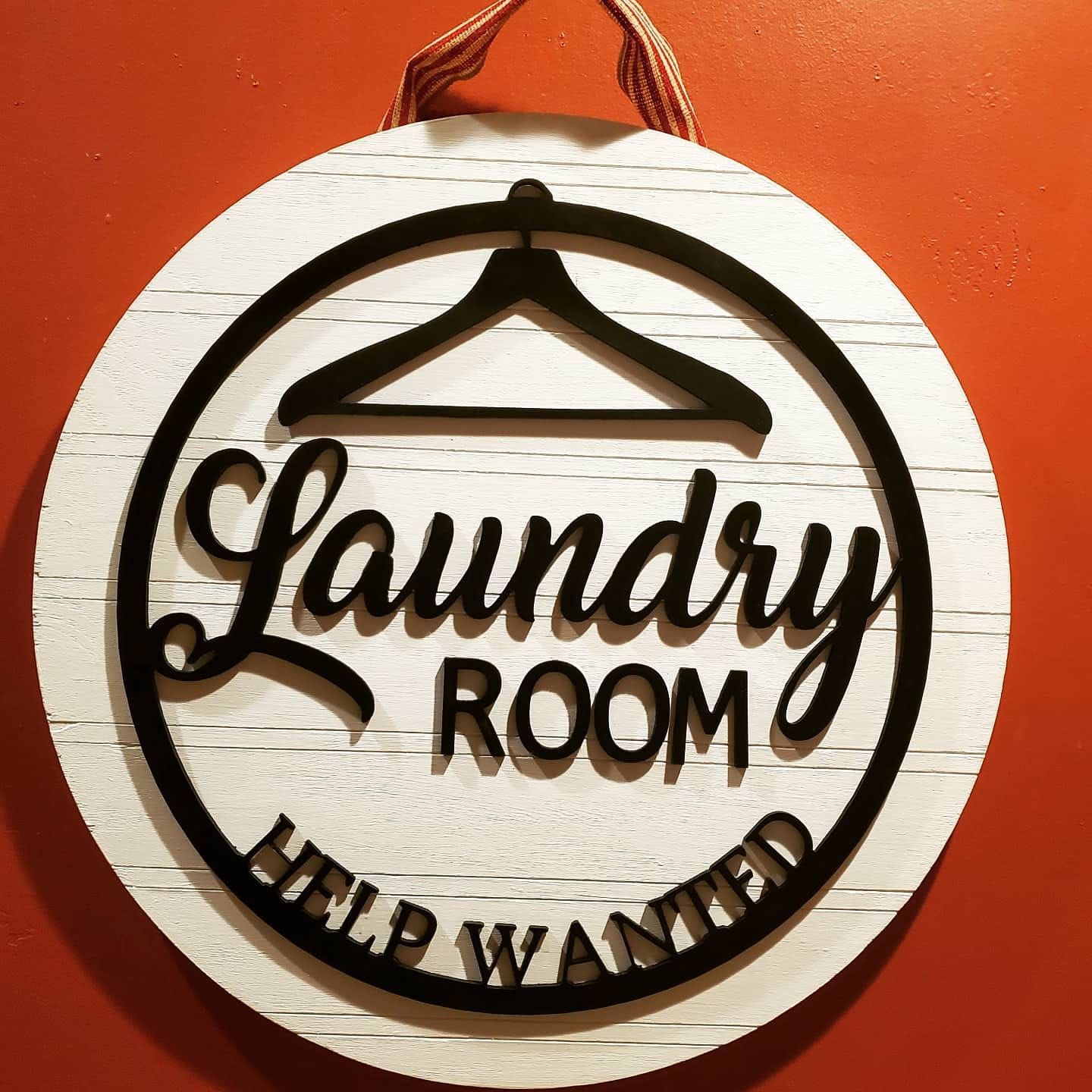 Laundry room sign with black text and hanger, white wooden background, red wall.