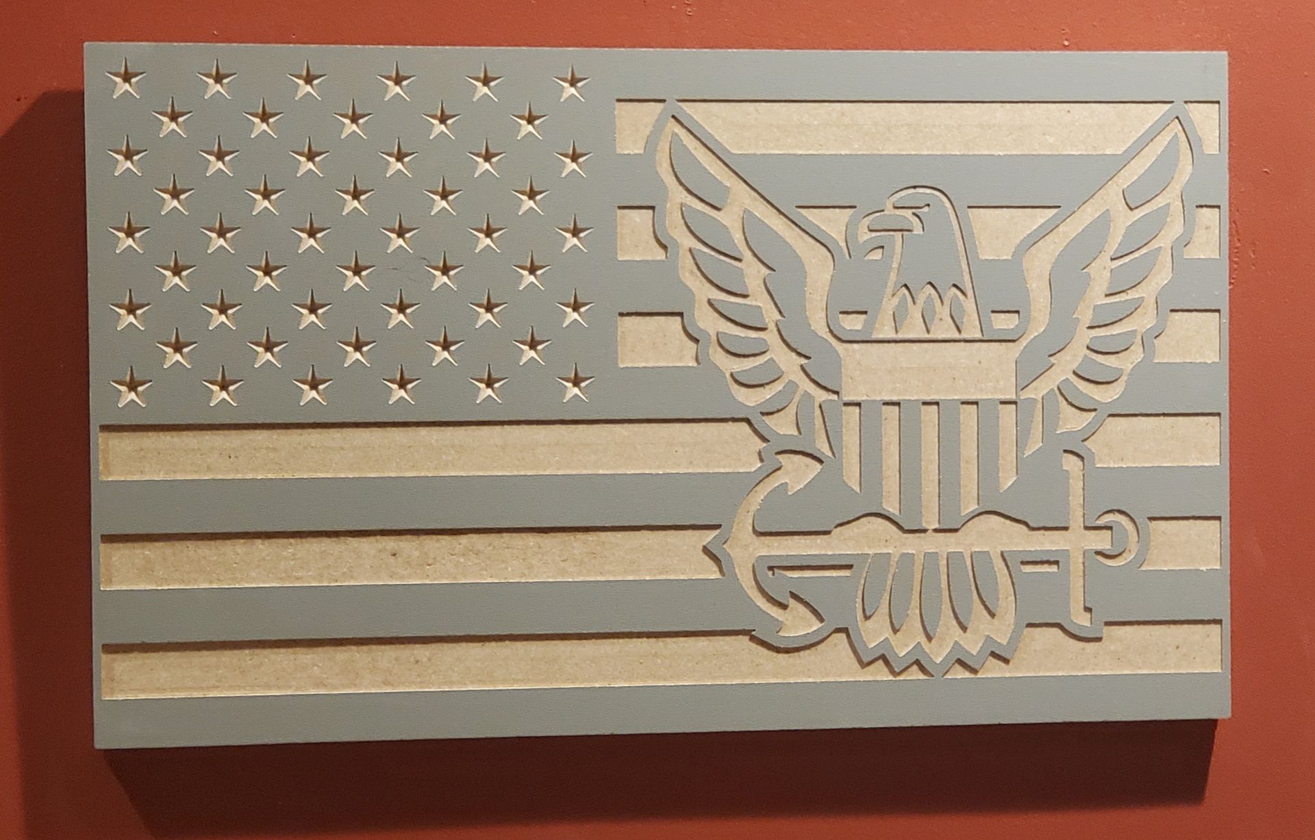Wooden carved American flag with eagle emblem. Gray and tan colors, mounted on a red wall.