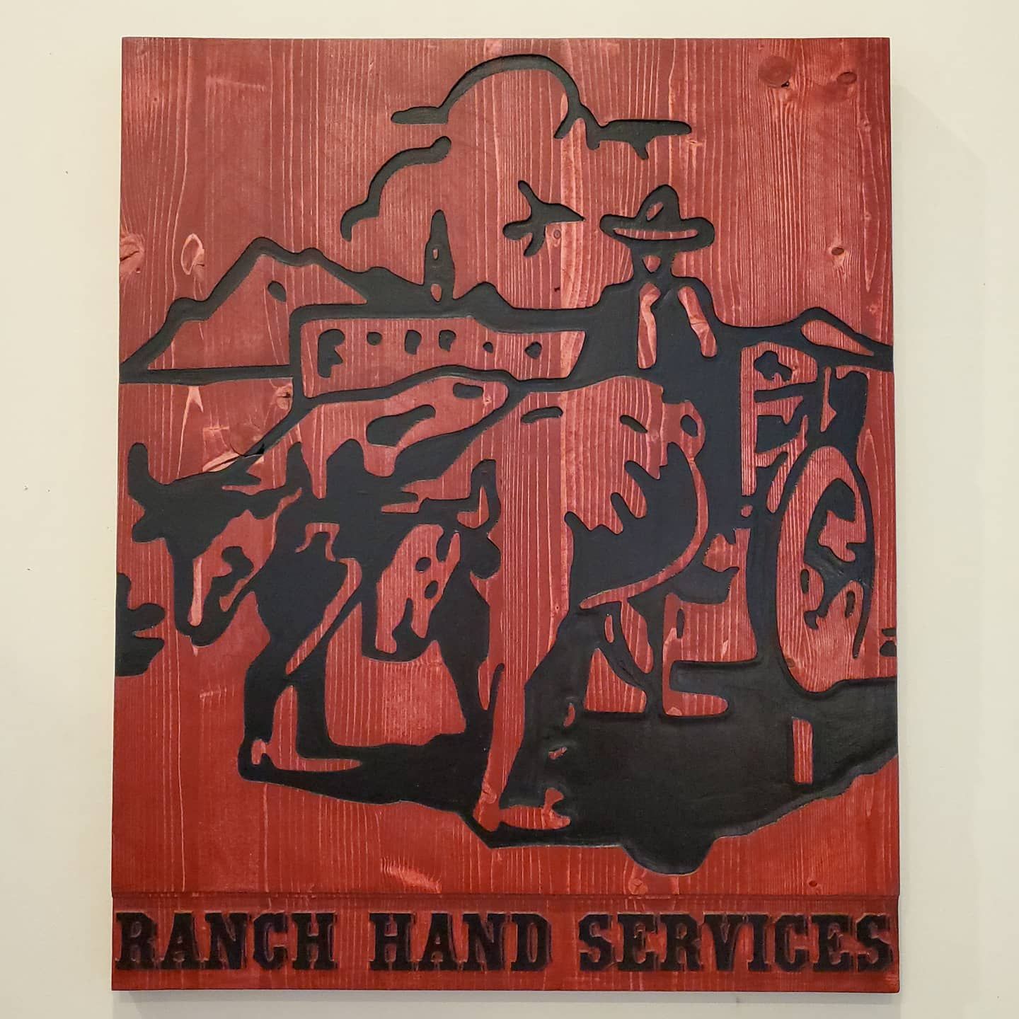 Rustic wooden sign with a cowboy and cattle in black silhouette on red background. Text:
