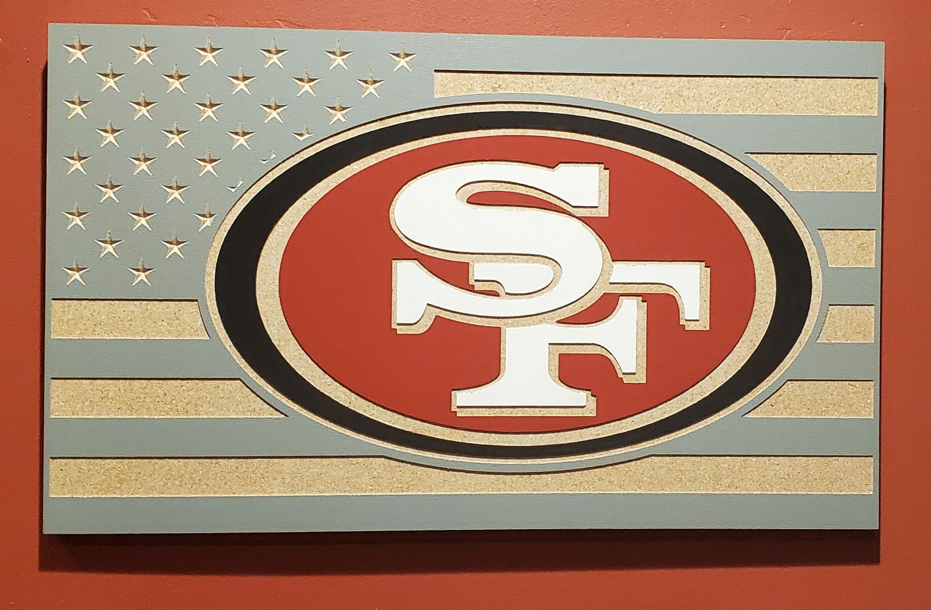 Wooden carving of the American flag with the San Francisco 49ers logo in the center. Red, gold, blue, and white colors.