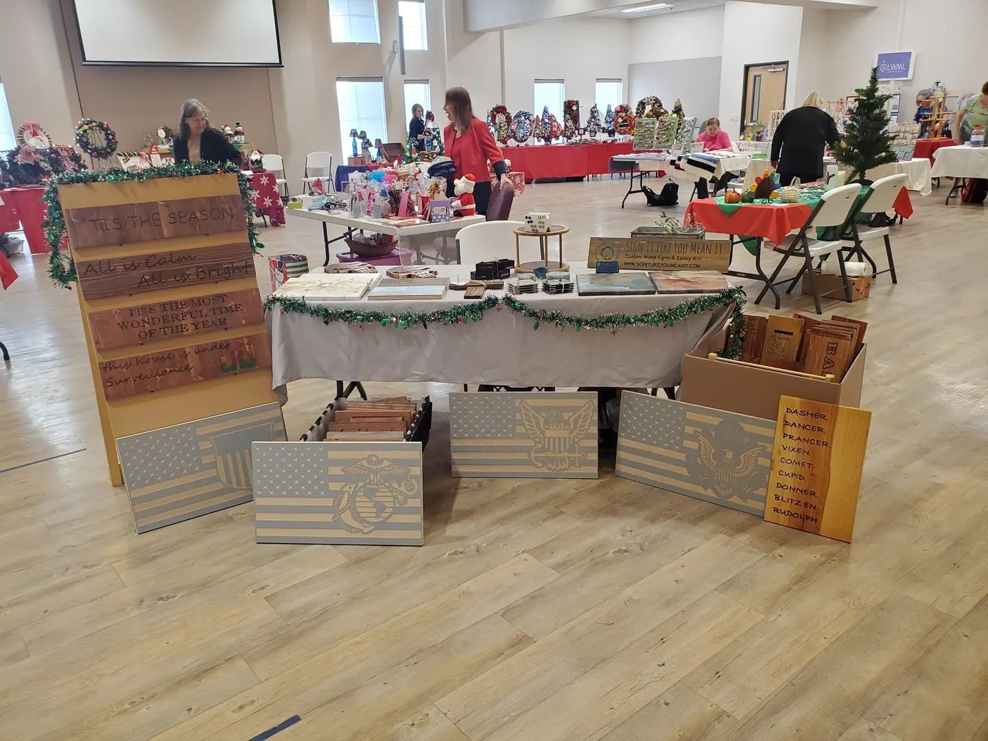 A craft fair with vendors displaying various handmade items, including wooden signs and crafts.